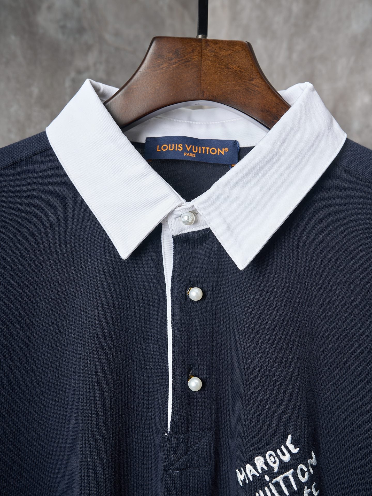 Navy polo shirt with white pointed collar, pearl-look buttons, and stitched placket detail