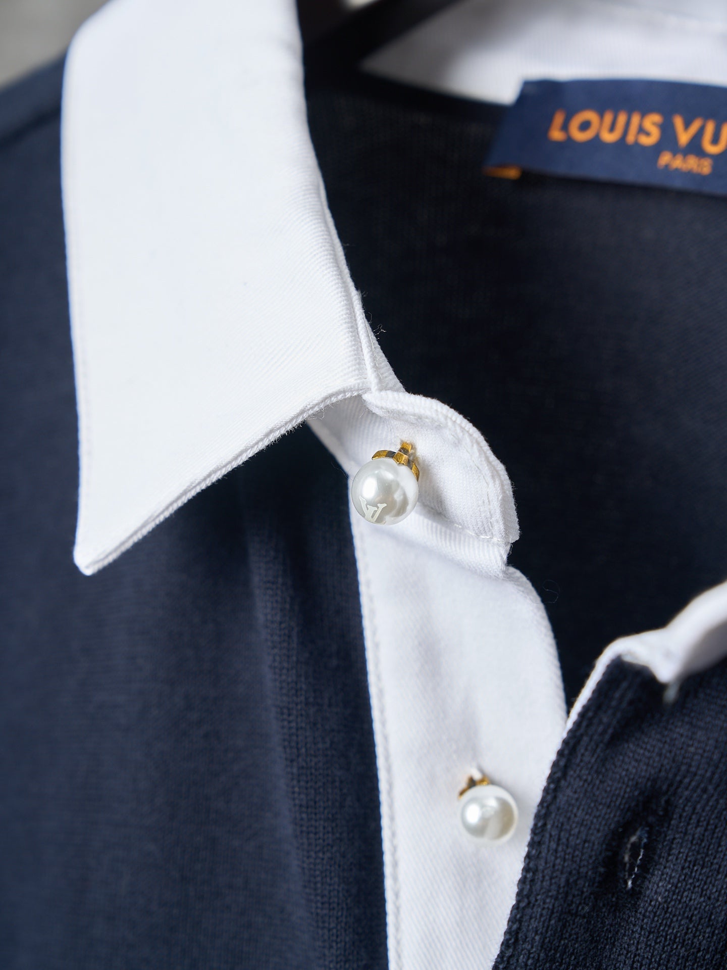Navy polo shirt with white collar and gold-tone clasp above pearl-look button