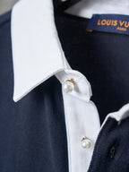 Navy polo with white collar edge and round pearl-style button at placket.