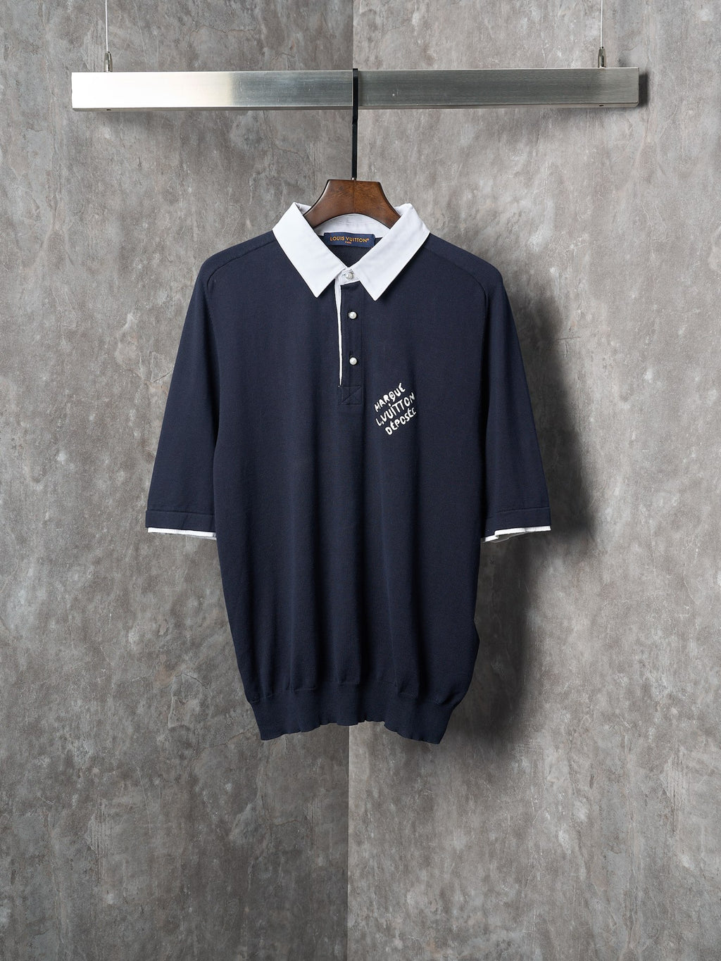 Navy polo shirt with white collar, three-button placket, and embroidered logo on chest
