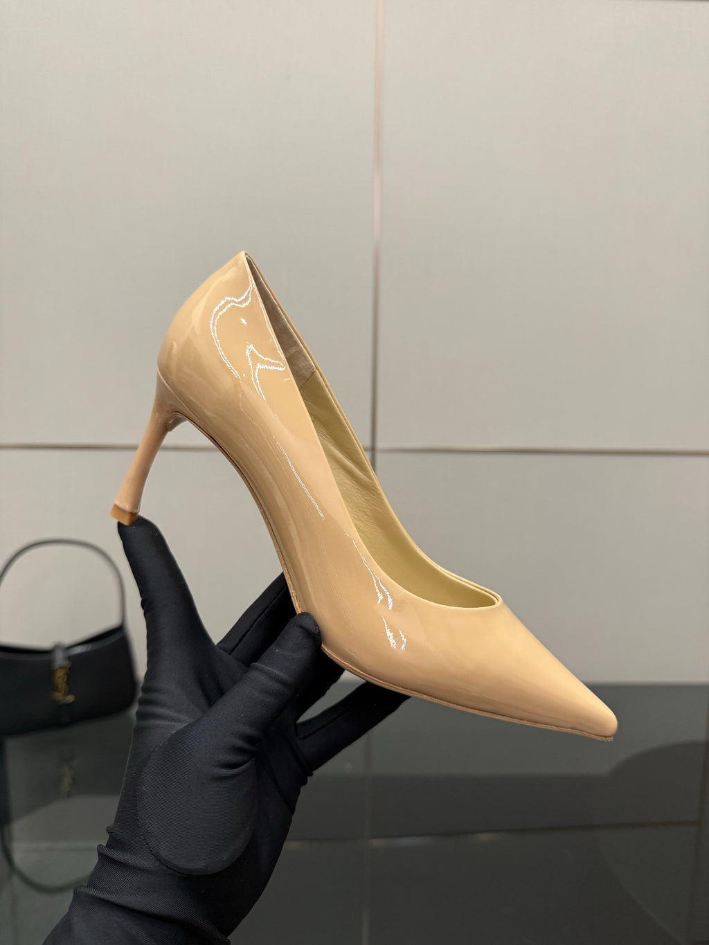 Beige patent pointed-toe pump on stiletto heel held in black glove