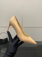 Beige patent pointed-toe pump on stiletto heel held in black glove