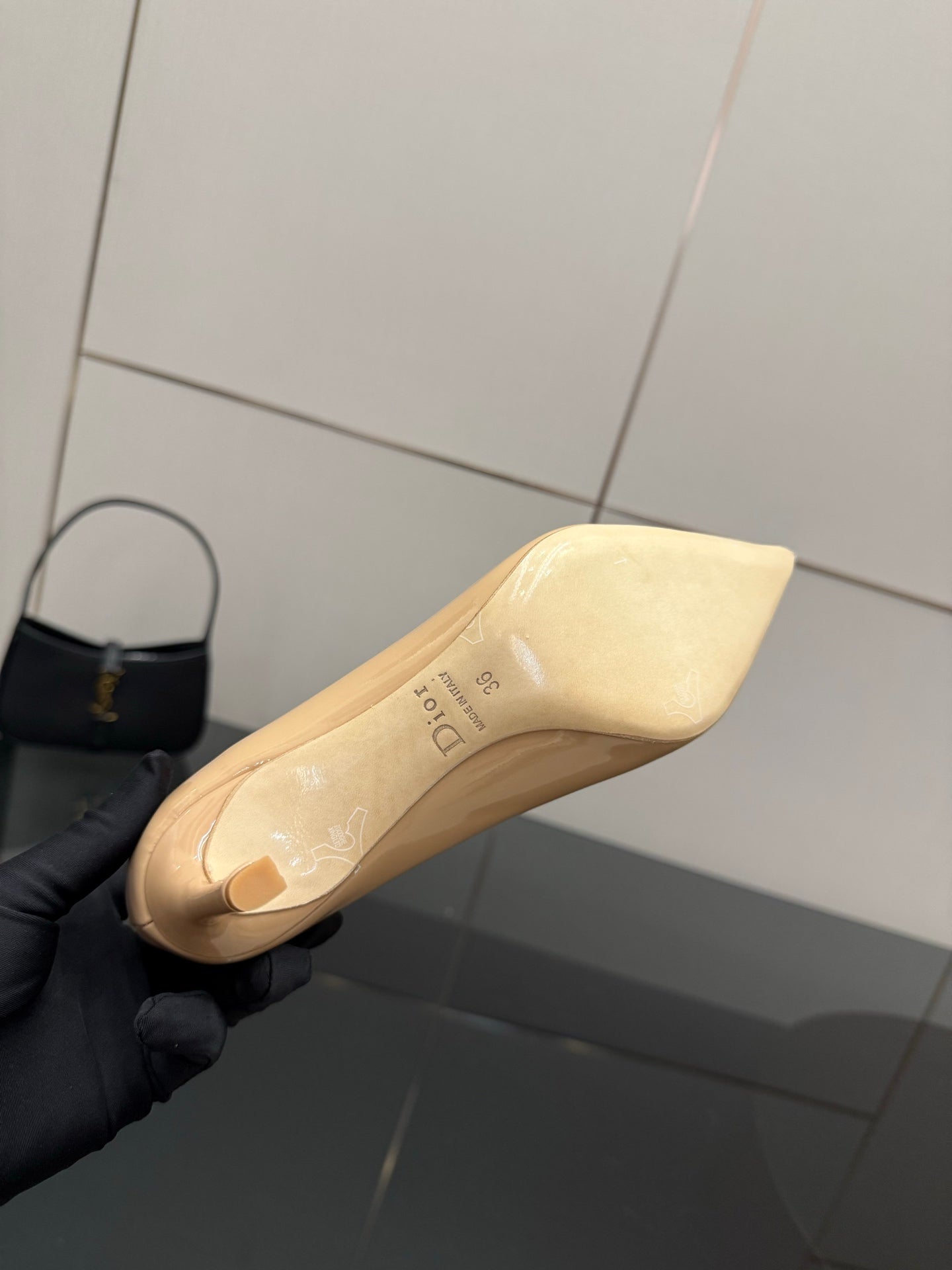 Beige patent pointed-toe pump sole and heel, held in black glove