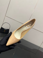 Beige patent pointed-toe pump with decorative strap, held in black glove