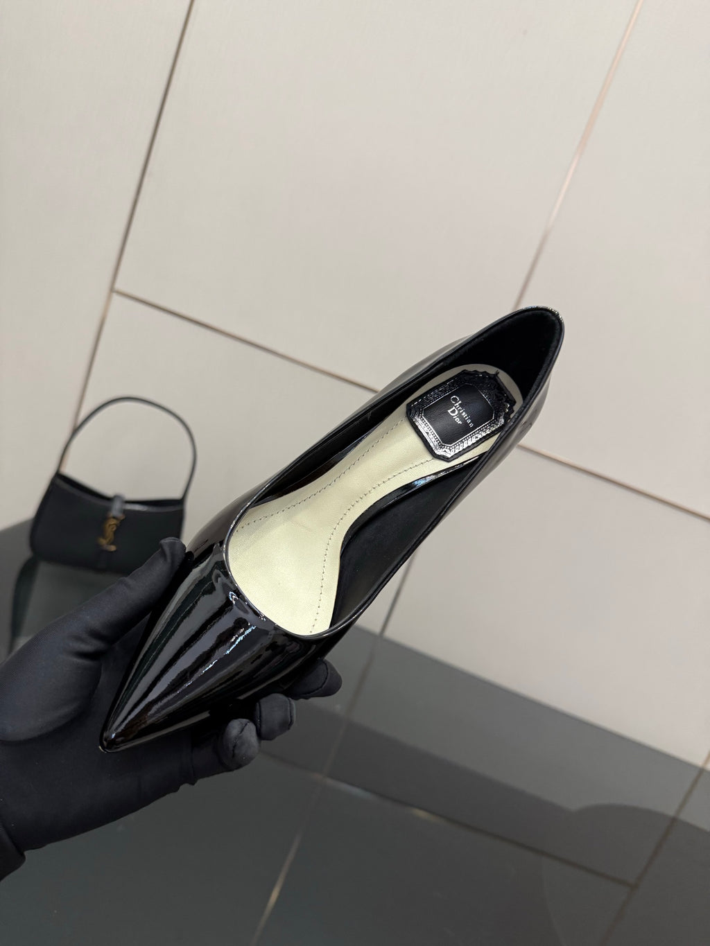 Black patent pointed-toe pump showing light insole, held in hand with glove