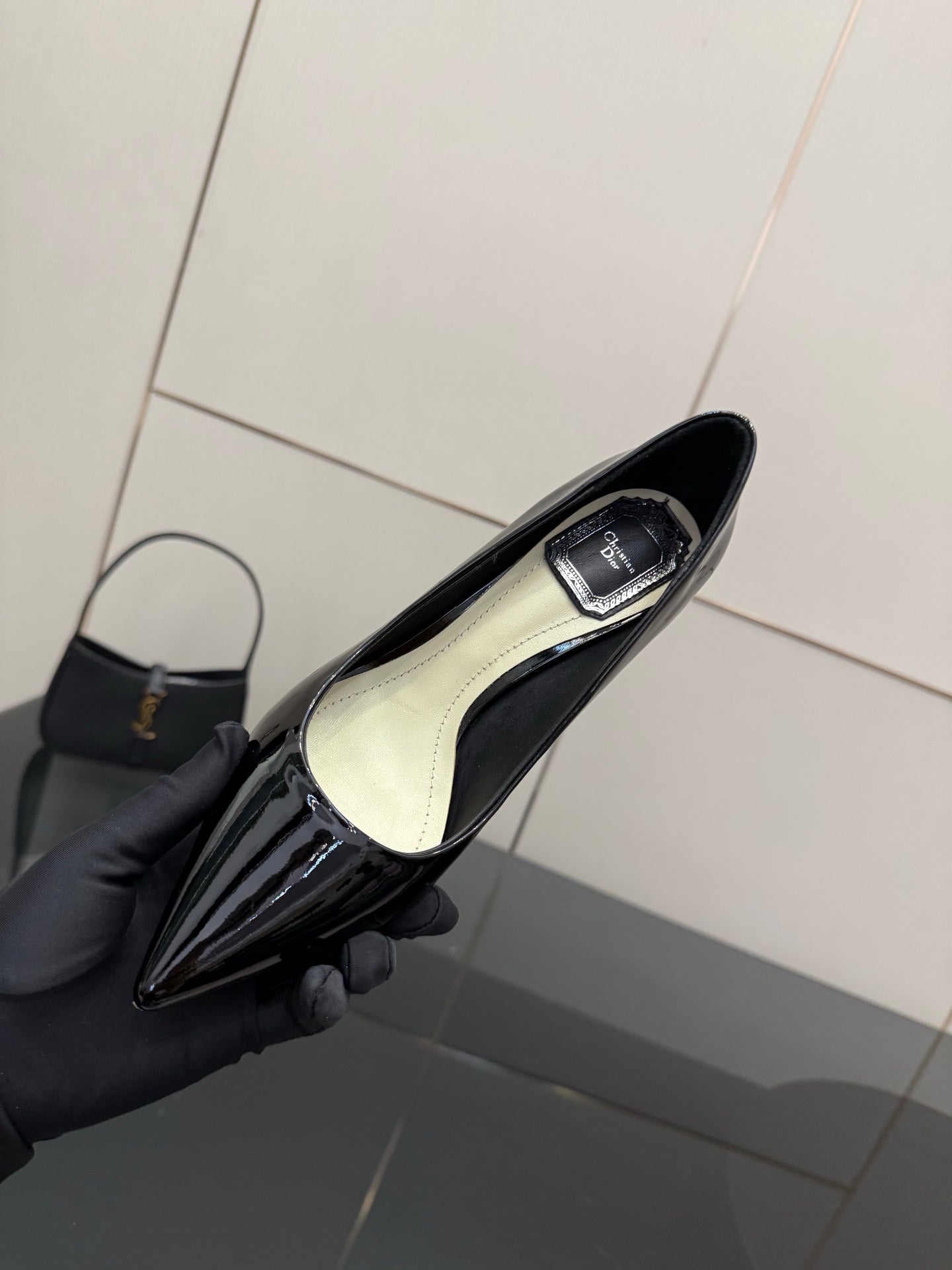 Black patent pointed-toe pump showing light insole, held in hand with glove