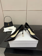 Black patent pointed-toe pumps with gold logo detail, angled pair on white box