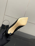 Black patent pump with beige insole, close-up held by gloved hand