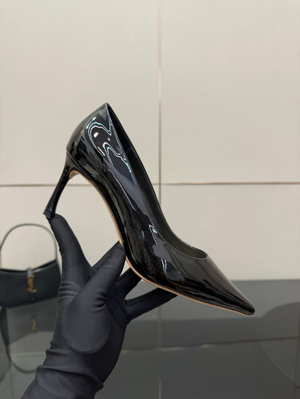 Black patent pointed-toe pump held in hand, close-up of heel and glossy upper