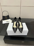 Black patent pointed-toe pump heels with gold logo, shown as a pair on white boxes