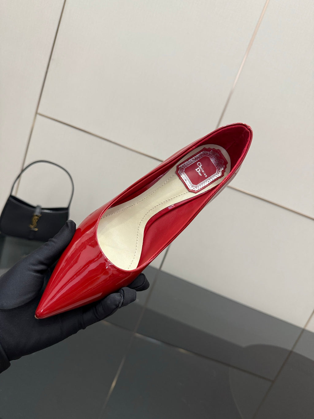 Red patent pointed-toe pump with insole detail, held in a dark glove