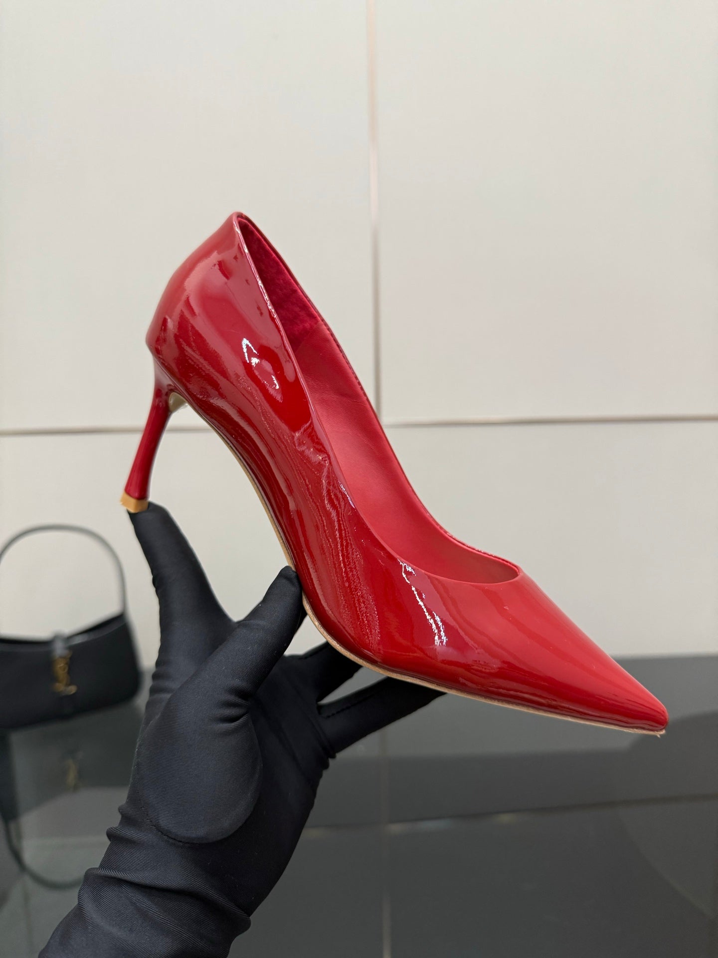 Red patent pointed-toe pump with stiletto heel, held in a dark glove