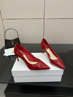 Red patent pointed-toe pumps with stiletto heels, angled side view on boxes