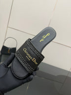 Black leather slide sandal held in hand; textured strap with gold Christian Dior branding