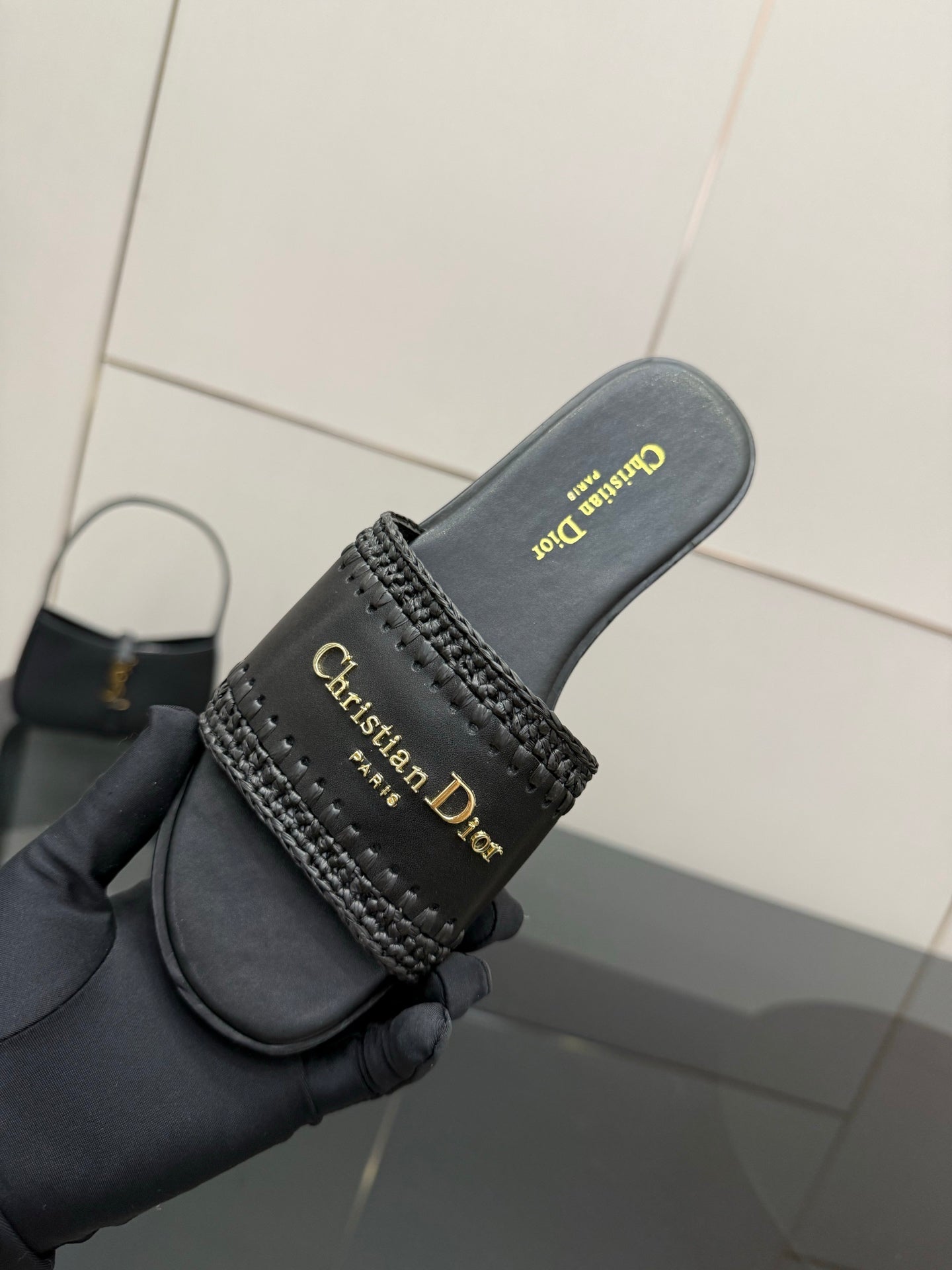 Black leather slide sandal held in hand; textured strap with gold Christian Dior branding