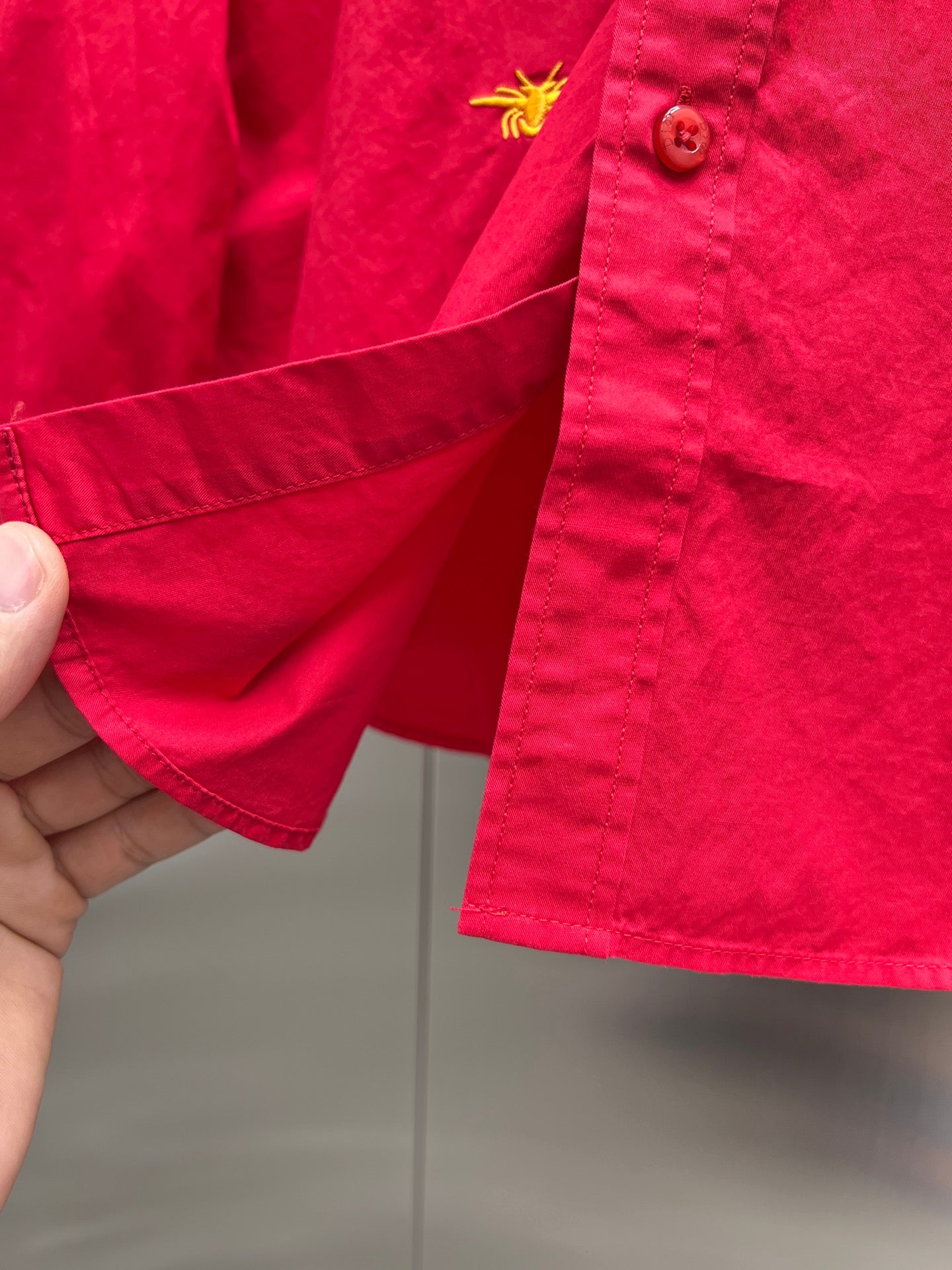 Red long-sleeve shirt sleeve cuff with button and yellow emblem
