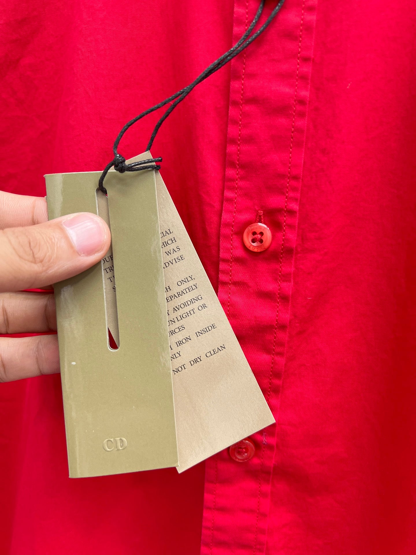 Red long-sleeve shirt with hanging beige product tags on black string