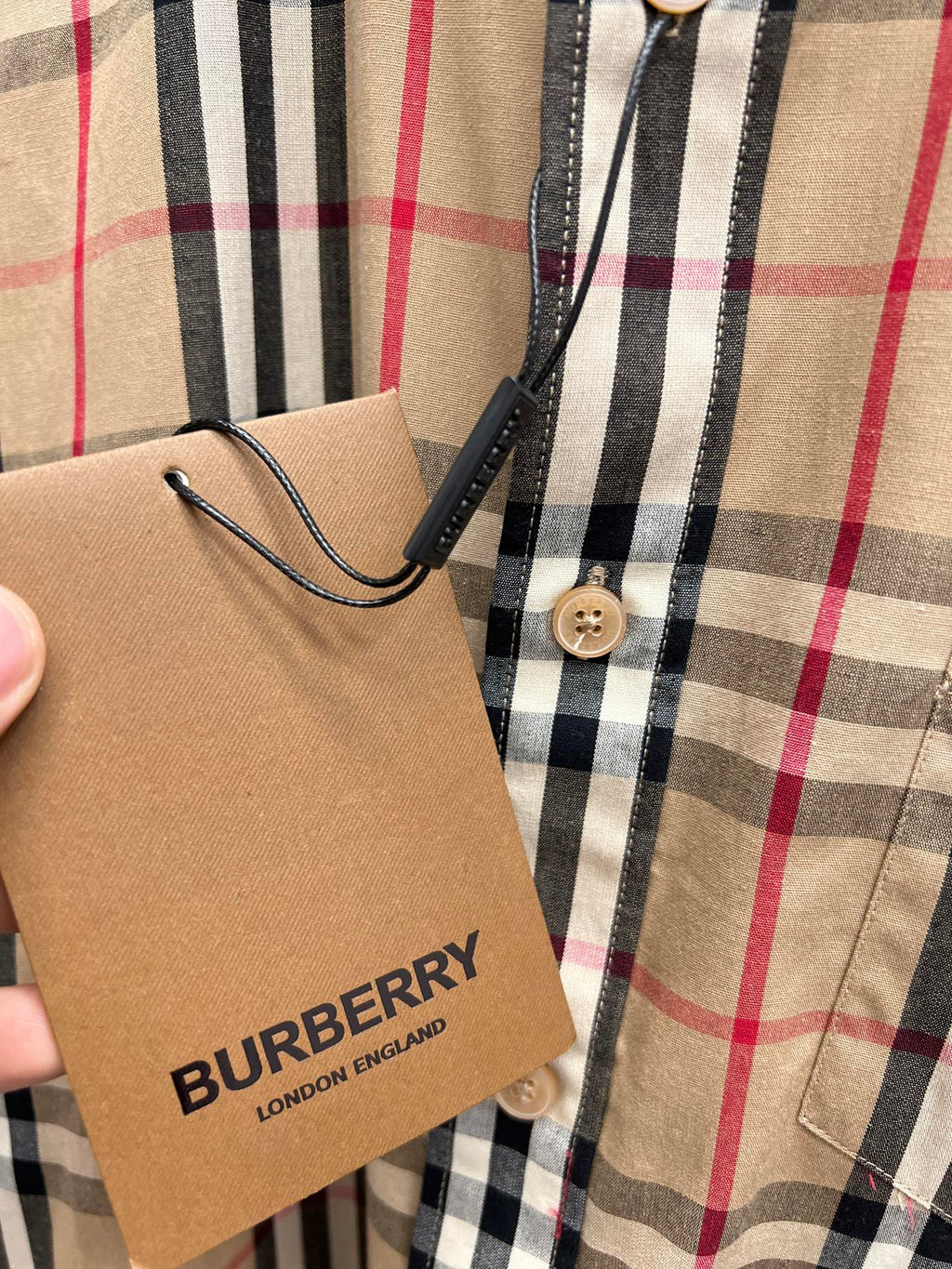 Burberry plaid shirt detail with price tag and buttoned pocket area on beige