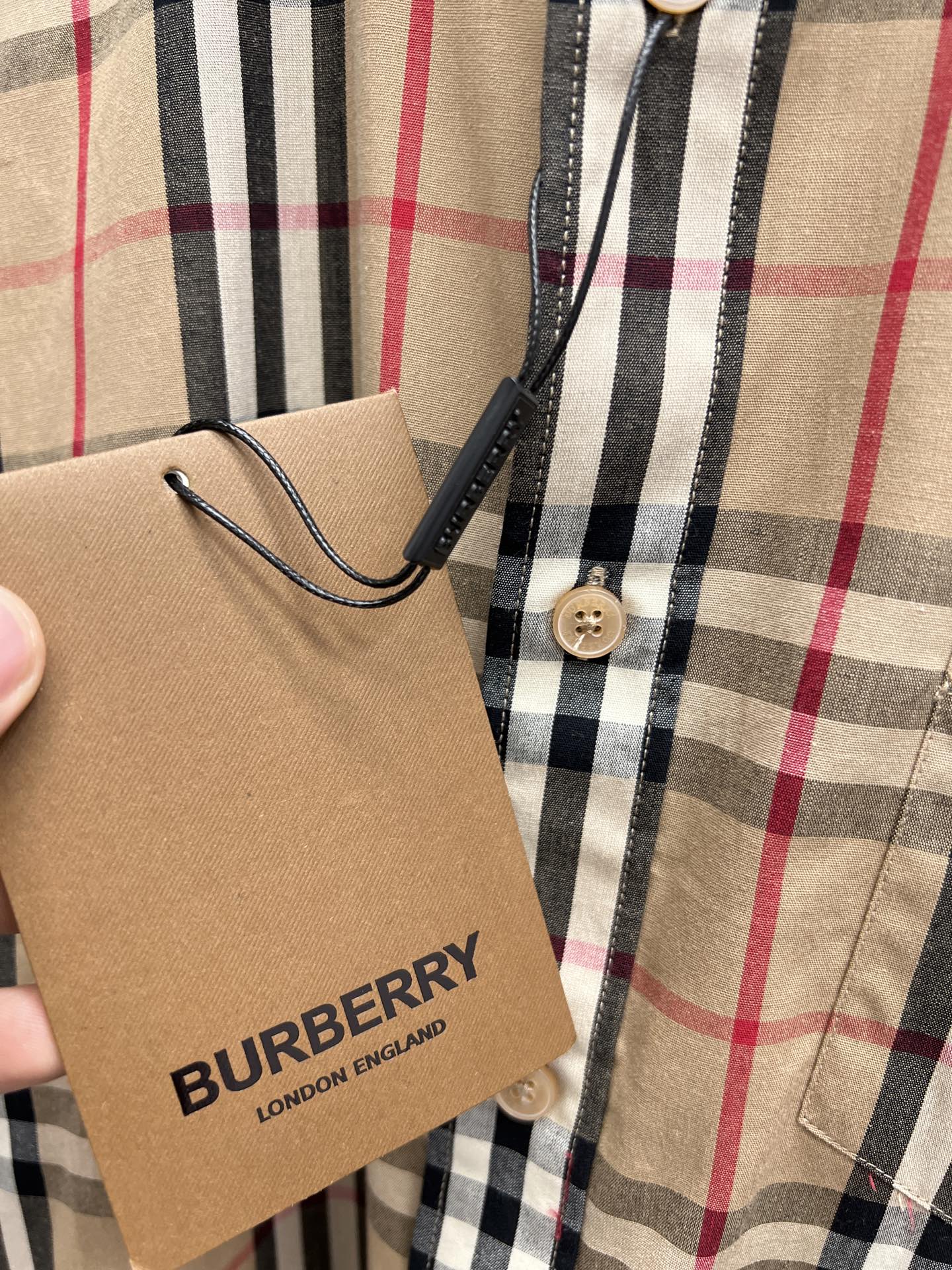 Burberry plaid shirt detail with price tag and buttoned pocket area on beige