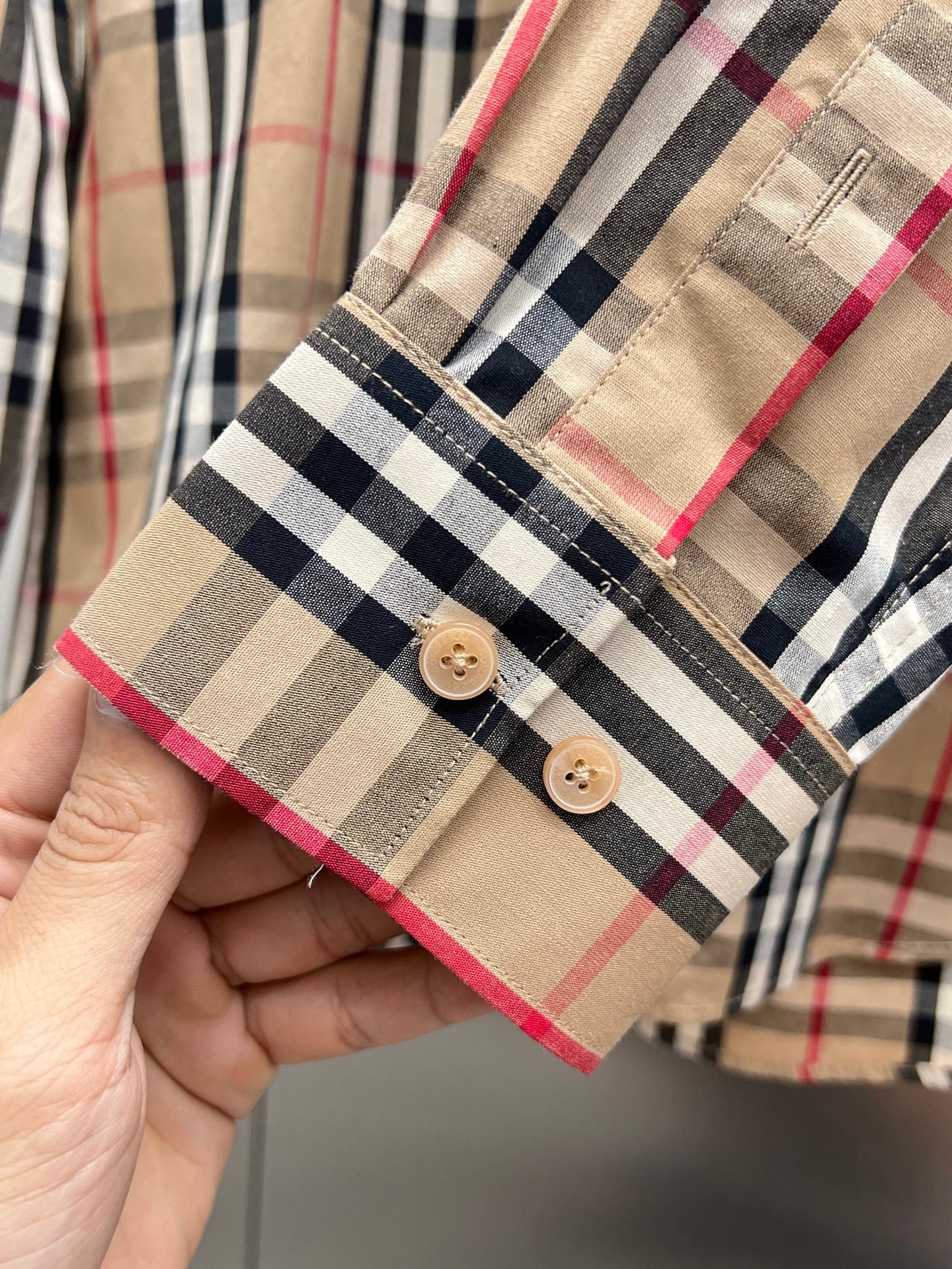 Plaid button-up shirt cuff with two tan buttons and red/blue/white checks