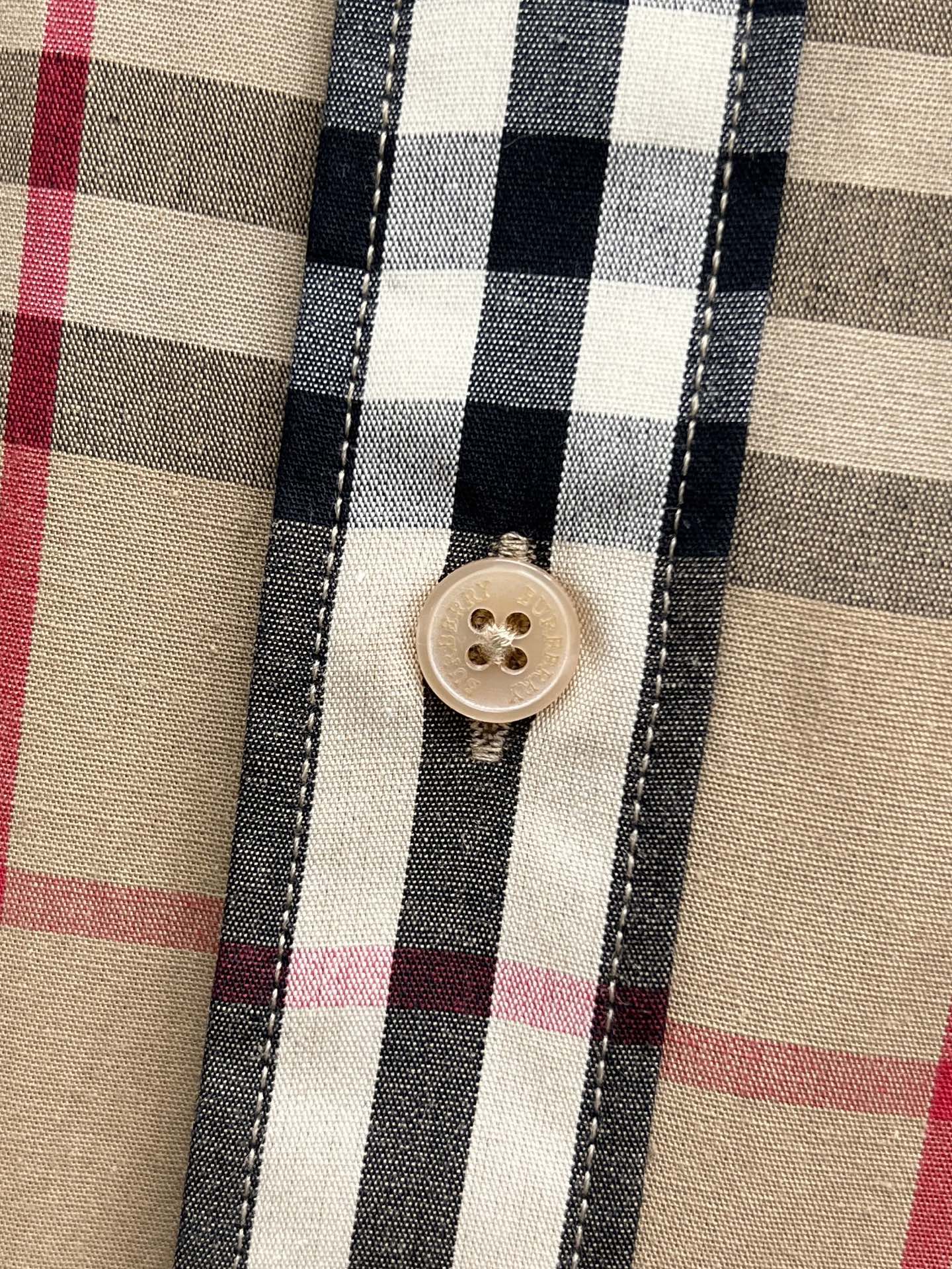 Burberry plaid shirt button close-up on beige fabric with navy and red lines