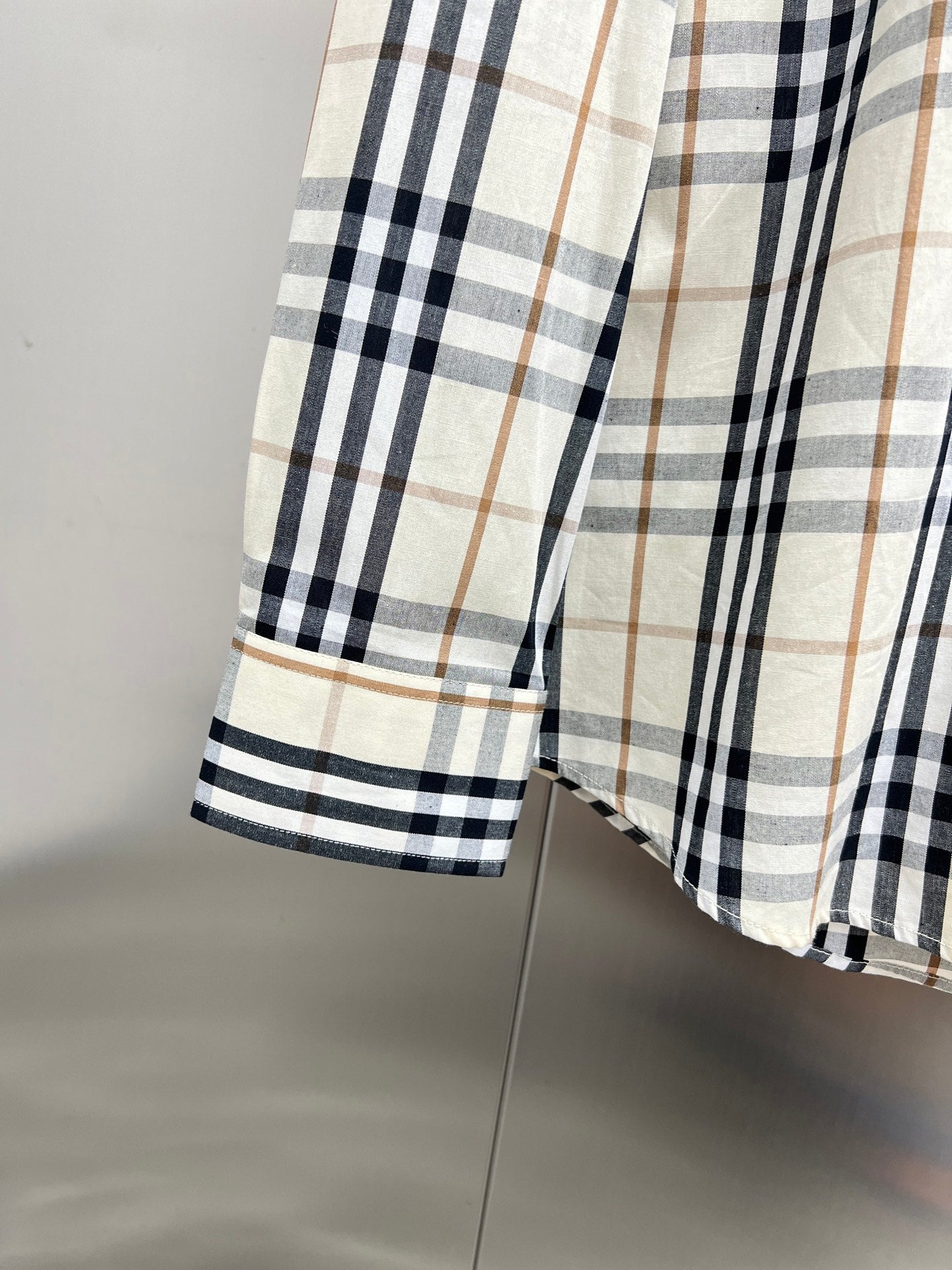 Plaid shirt cuff on long-sleeve button-up, cream with navy and tan checks.