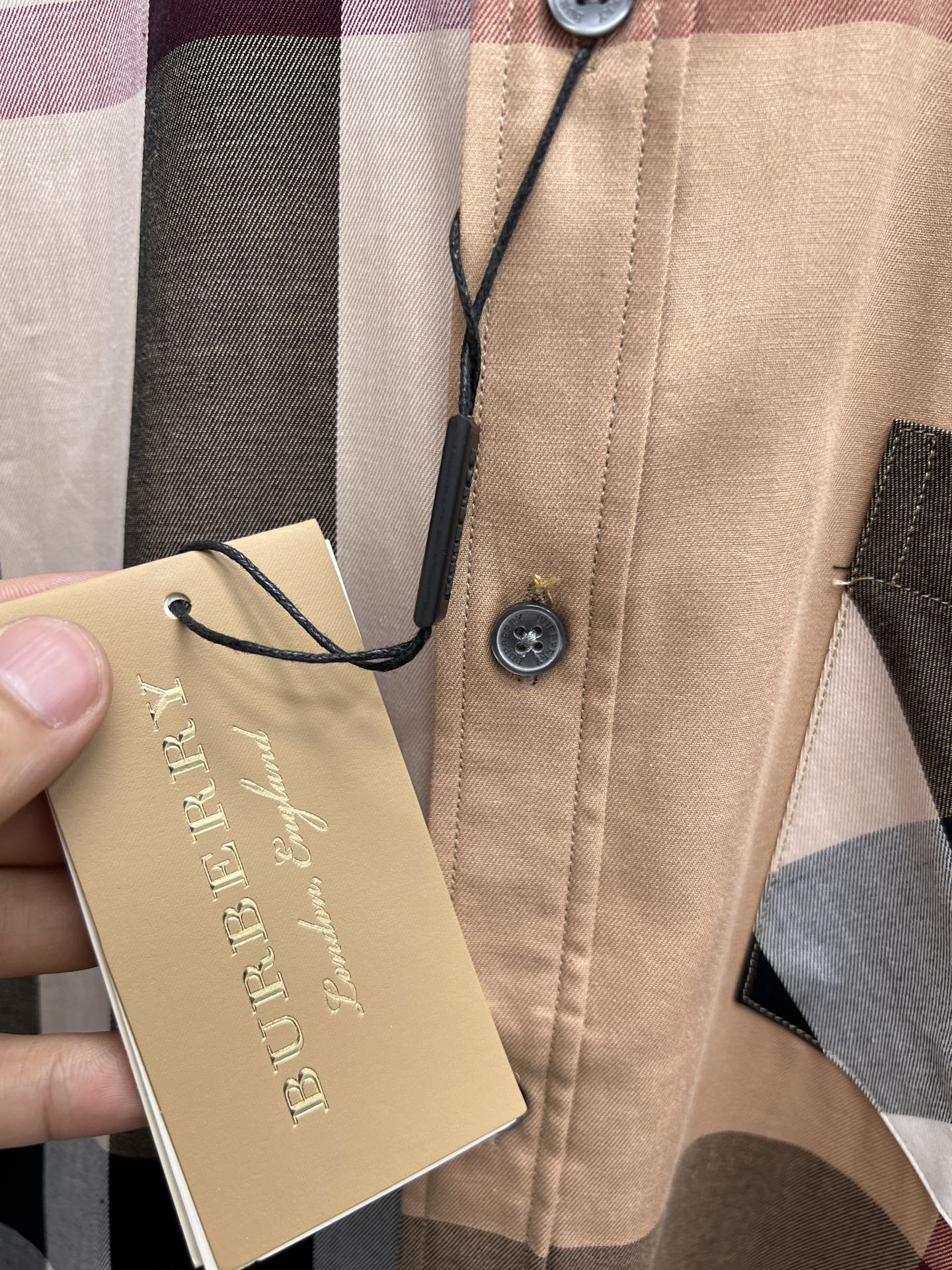 Beige plaid button-up shirt with hang tag attached to button placket