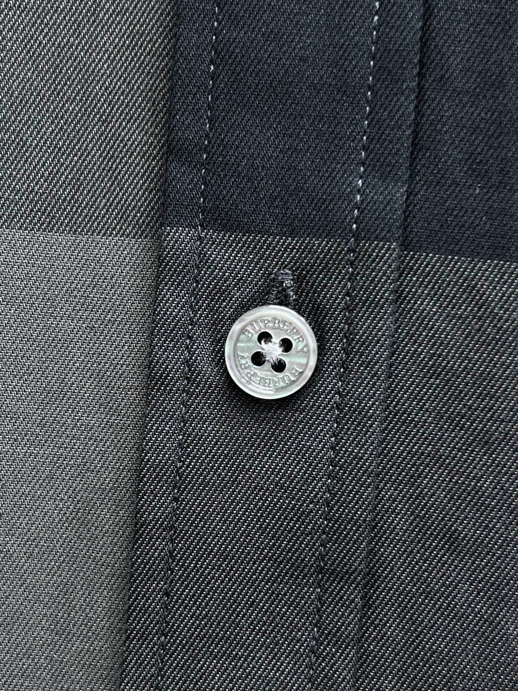 Burberry check shirt button and stitched placket detail on dark blue-gray fabric