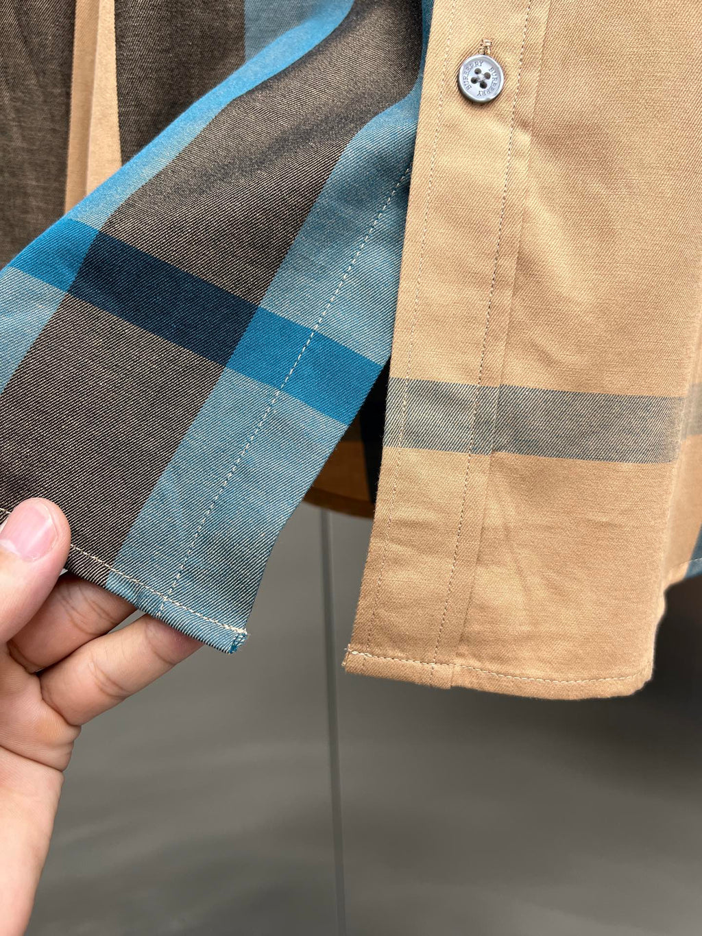 Check-pattern long shirt cuff on tan fabric with blue and dark stripes and button tab