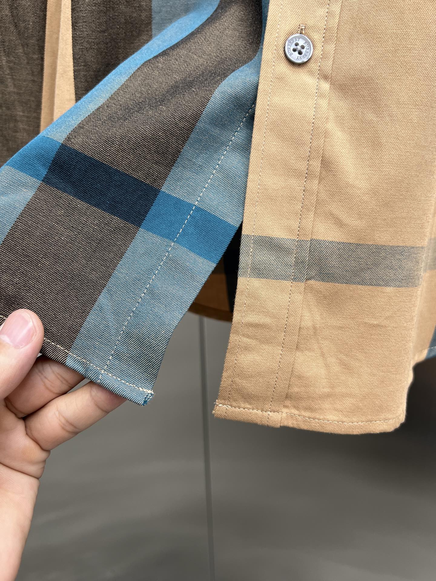 Check-pattern long shirt cuff on tan fabric with blue and dark stripes and button tab