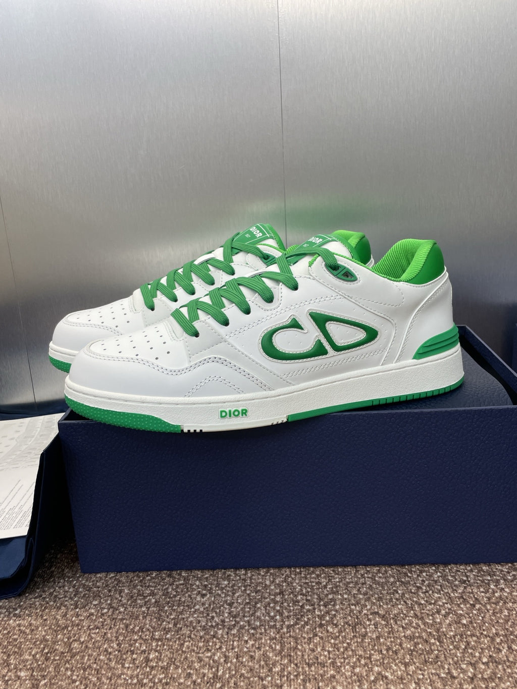White low-top sneakers with green laces and side CD-style logo detail