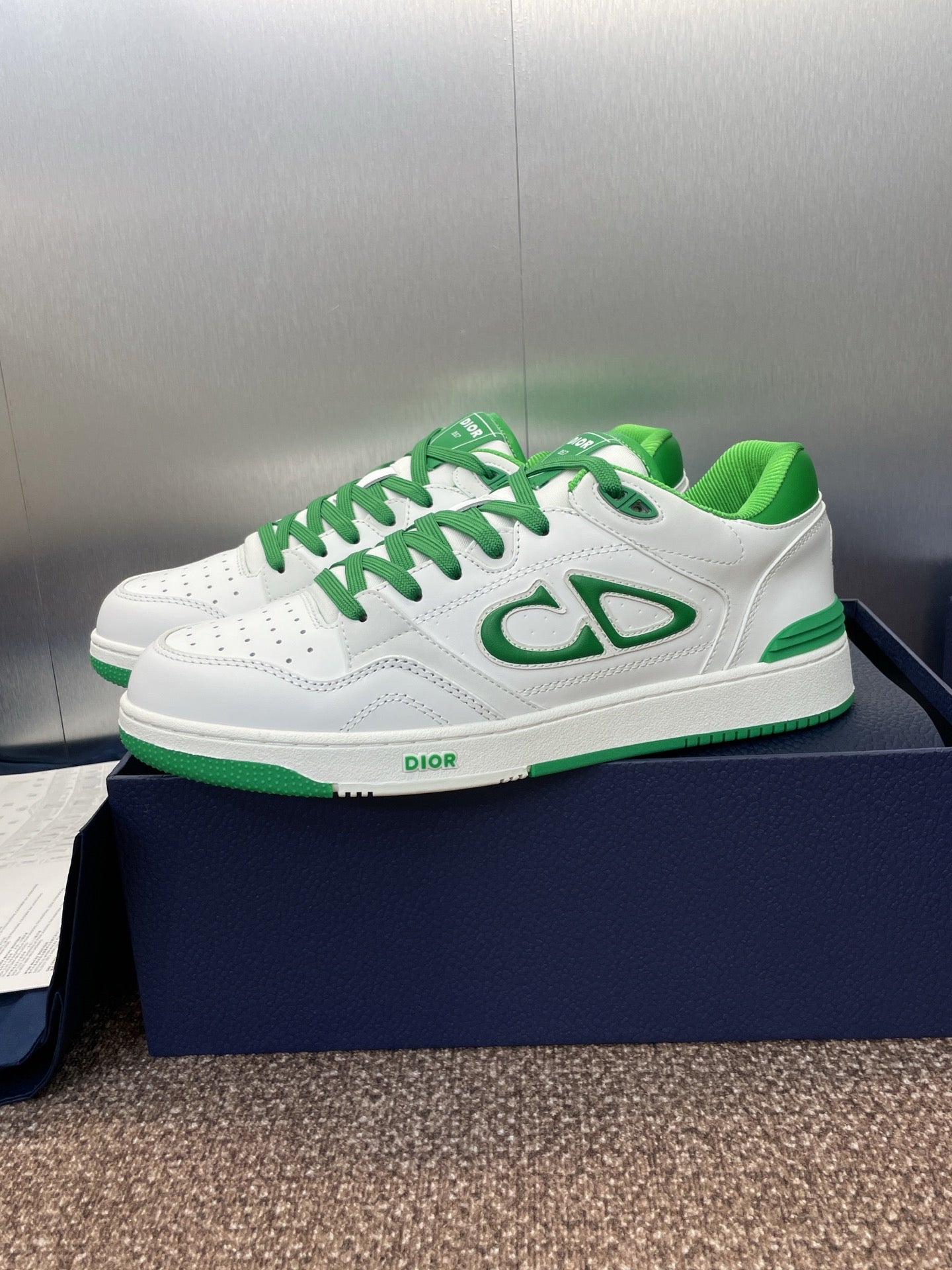 White low-top sneakers with green laces and side CD-style logo detail
