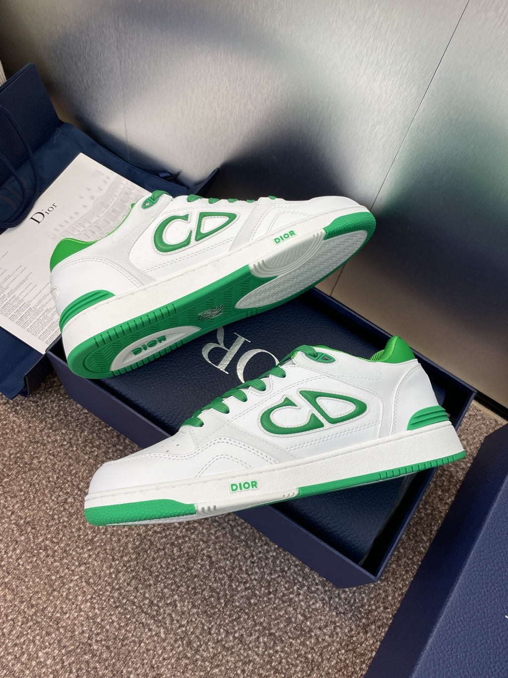 White low-top sneakers with green trim, CD-style side emblem, on navy boxes