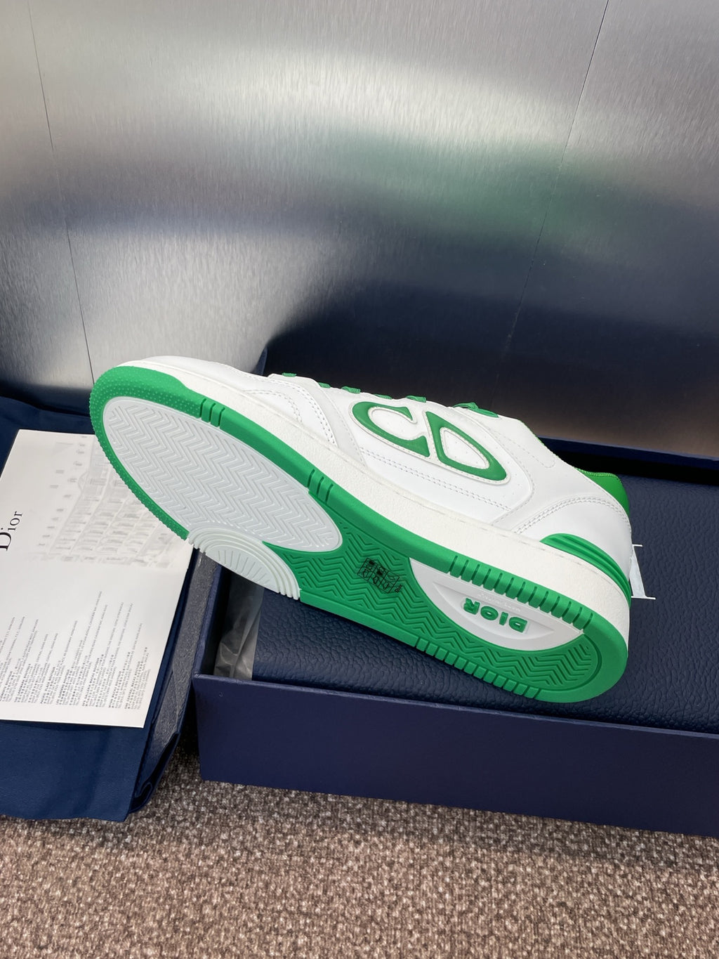 Shoe sole and side view of white low-top sneakers with green accents on box