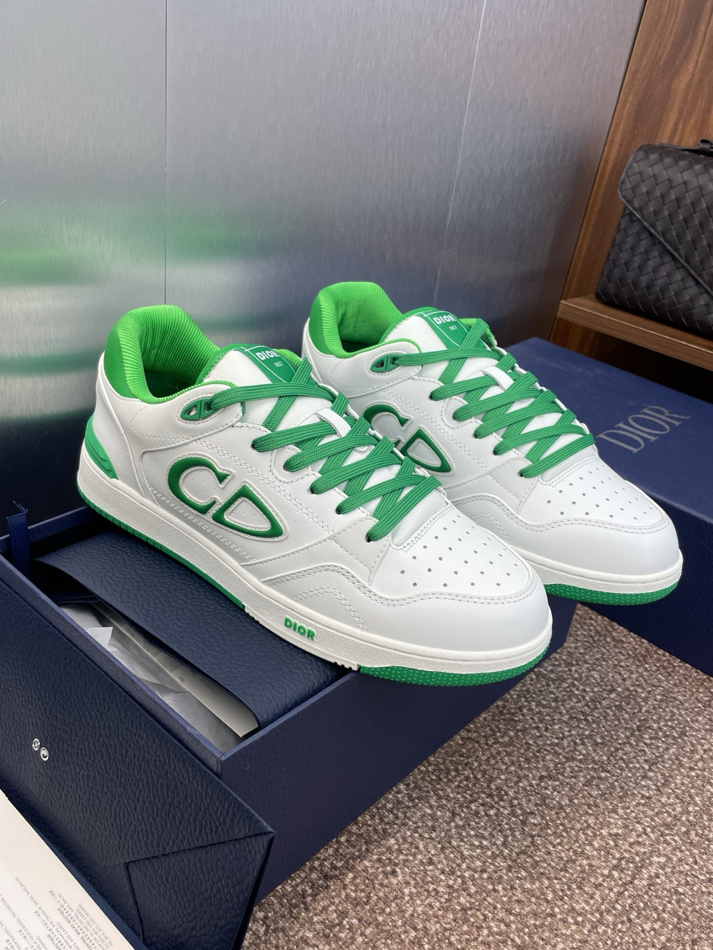 White low-top sneakers with green laces and signature CD-style logo detail