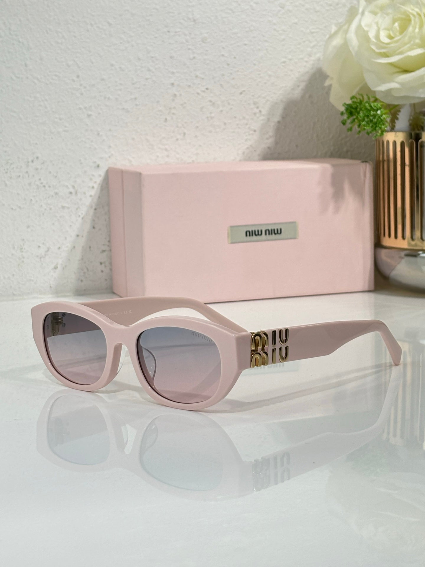 MiuMiu sunglasses with pale pink frames and blue-tinted lenses, gold logo on temples