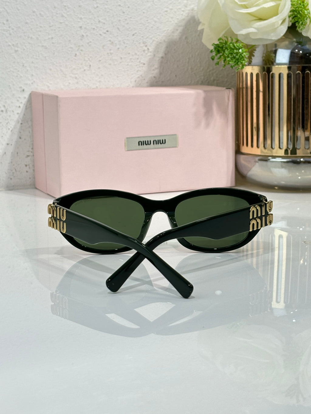 MiuMiu sunglasses with black frames and dark green lenses, gold logo across temple