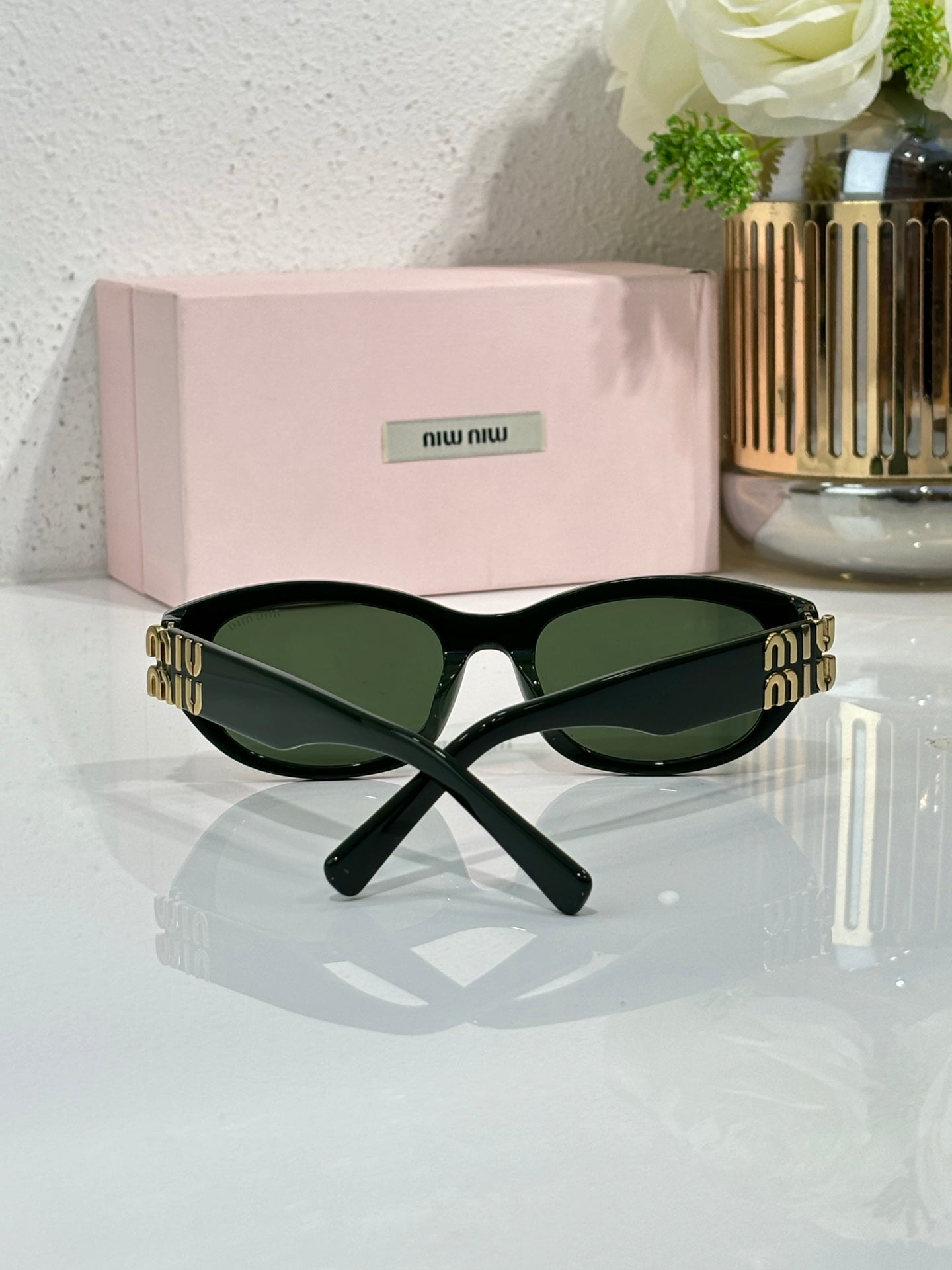 MiuMiu sunglasses with black frames and dark green lenses, gold logo across temple