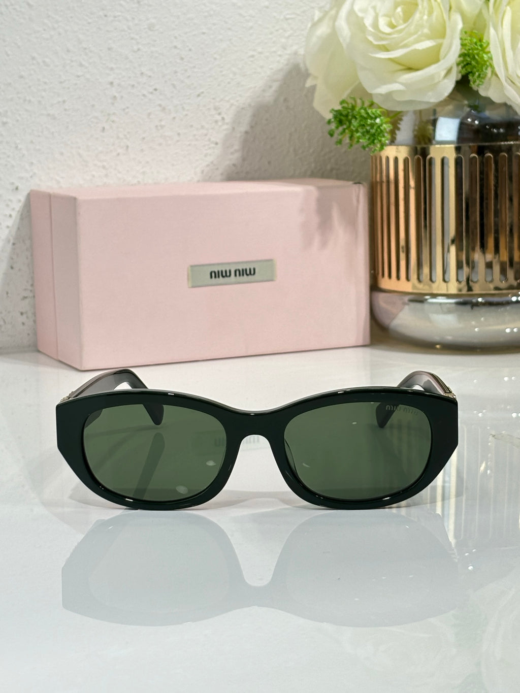 MiuMiu sunglasses with dark frames and green tinted lenses, curved oversized shape
