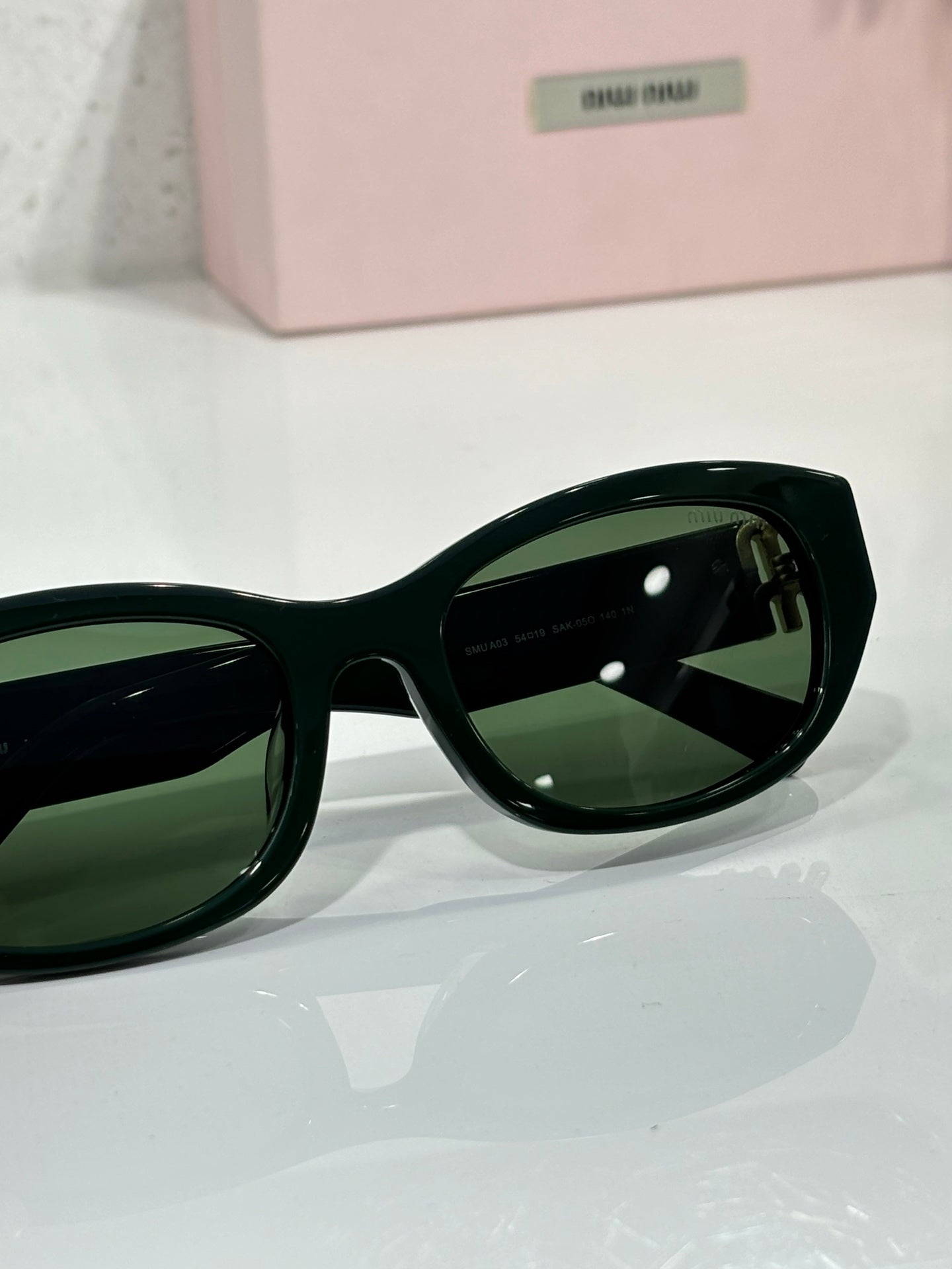 MiuMiu sunglasses close-up of green-tinted lenses and black frame with curved edges