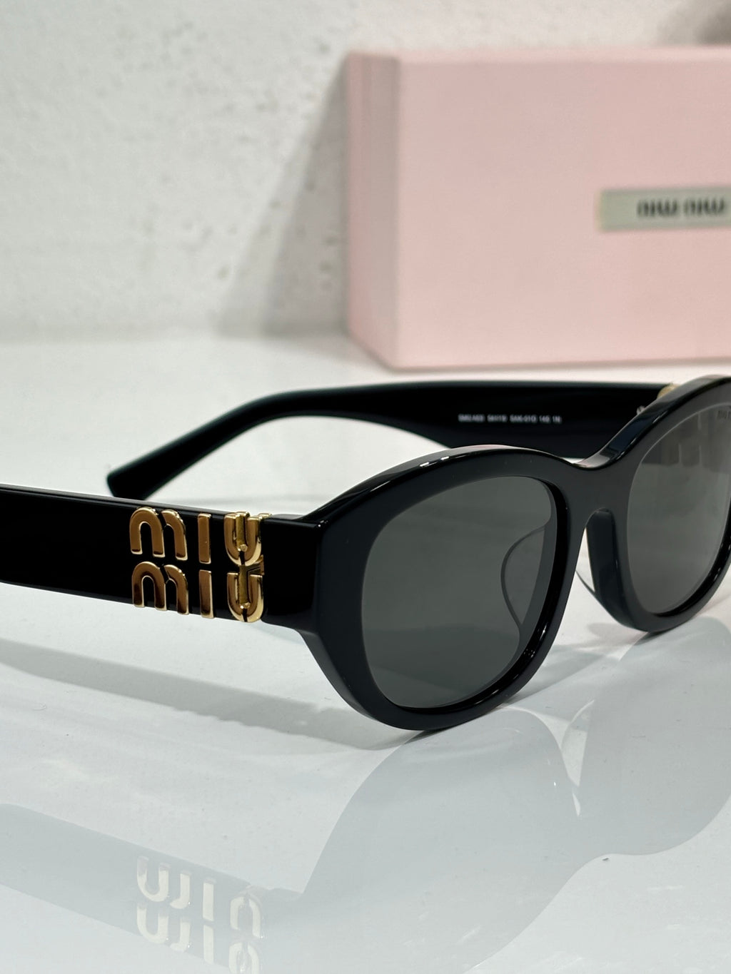 MiuMiu cat-eye sunglasses, angled view, black frames with gold Miu Miu emblem