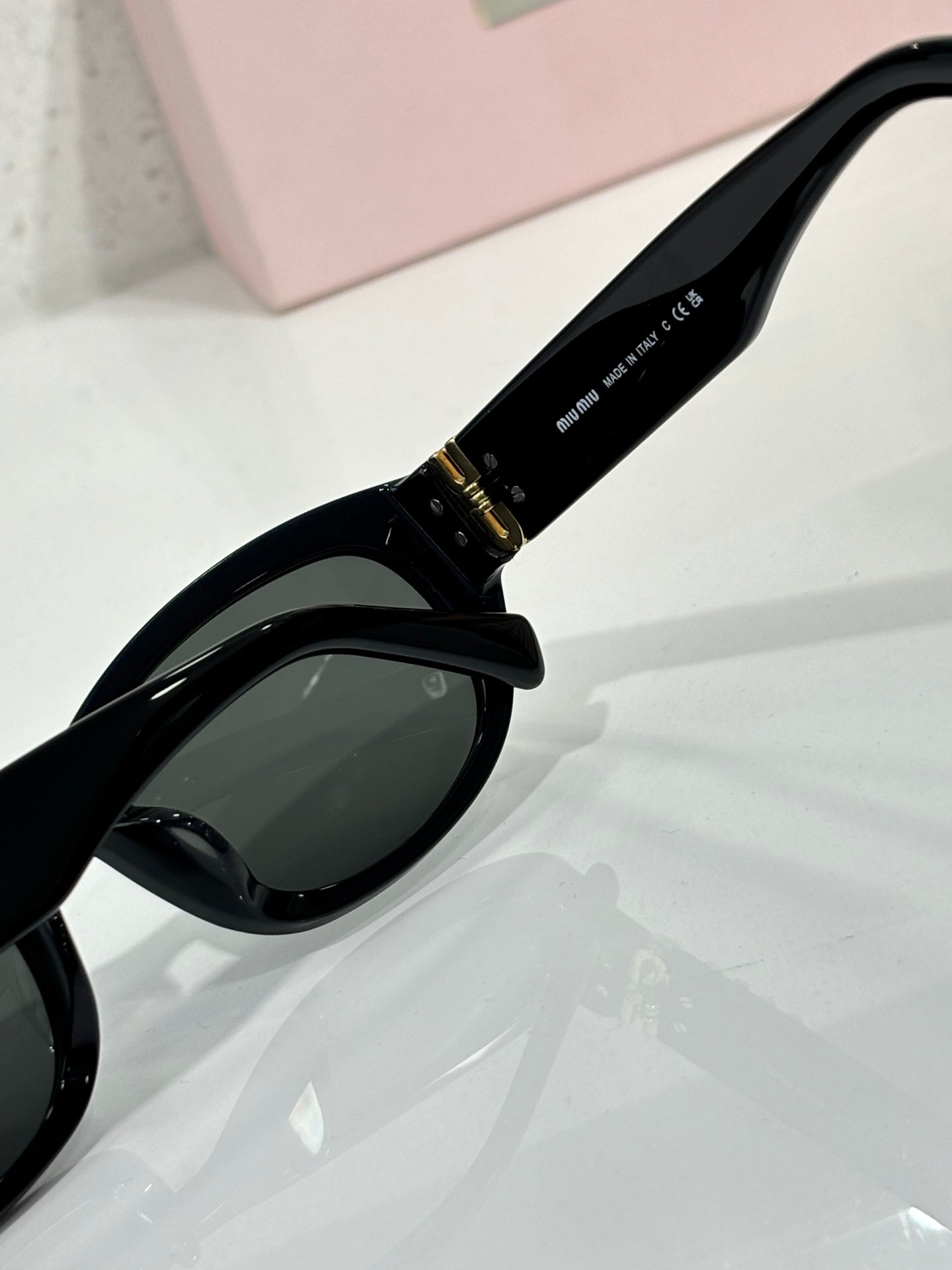 MiuMiu sunglasses temple close-up, black arm with gold logo and engraved text