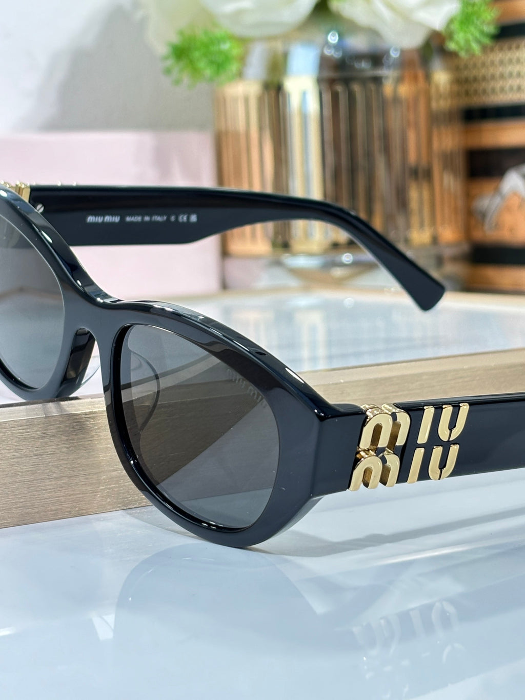 MiuMiu sunglasses profile view, black frame with gold Miu Miu logo on temple