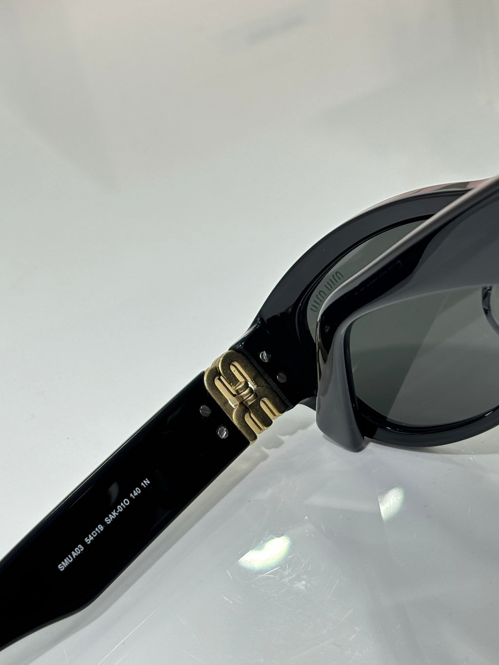 MiuMiu sunglasses temple close-up, black arm with gold clasp hardware