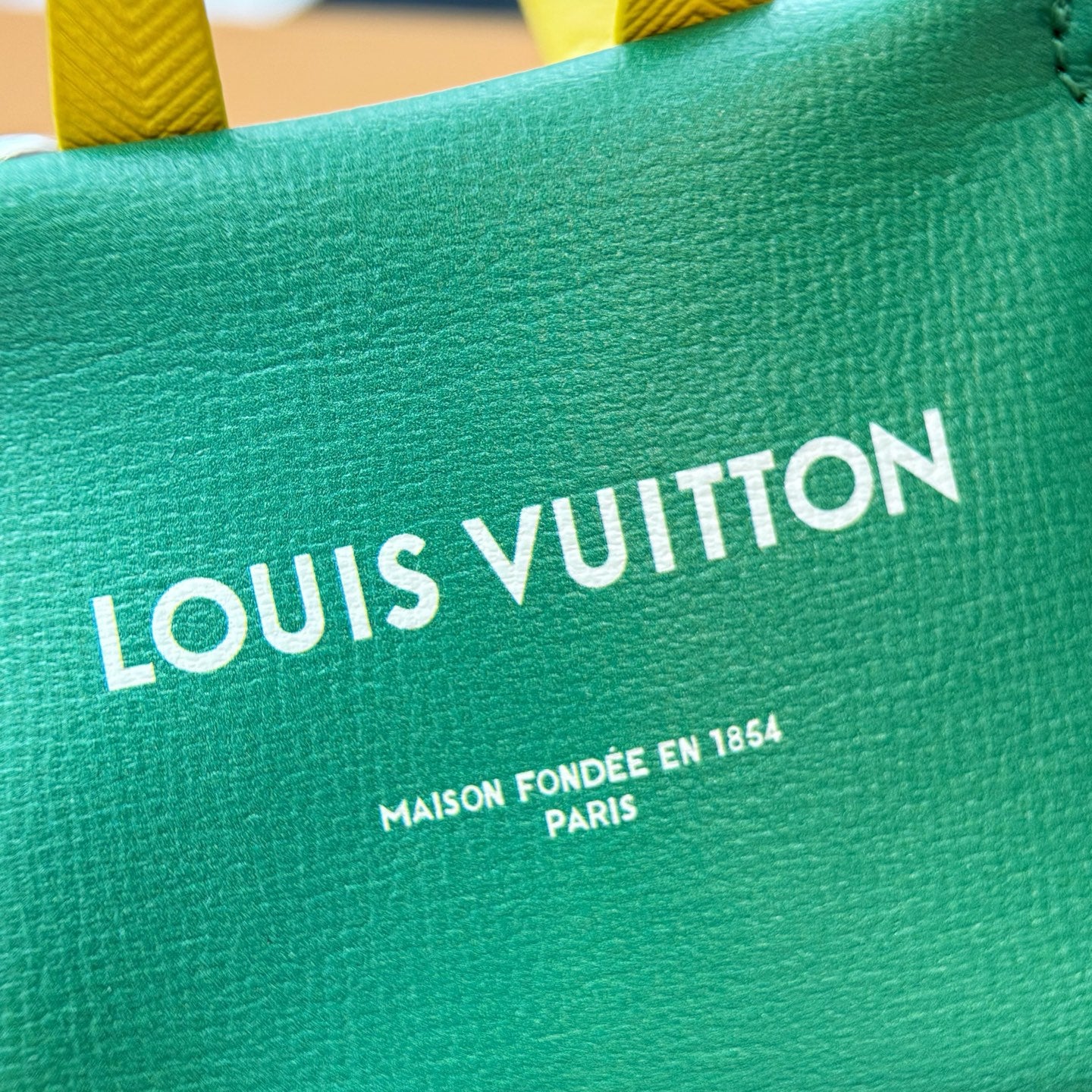 Louis Vuitton logo on green small bag front with yellow strap at the top edge