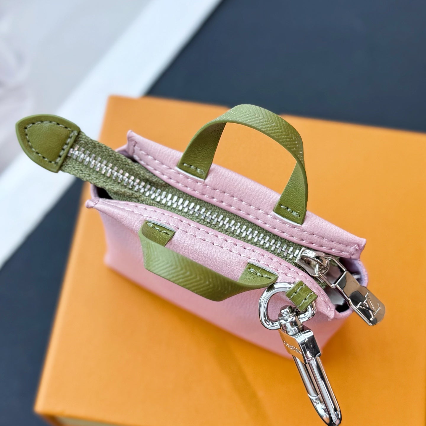 Pink small bag with green zip tape, silver zipper pull, and green handle straps.