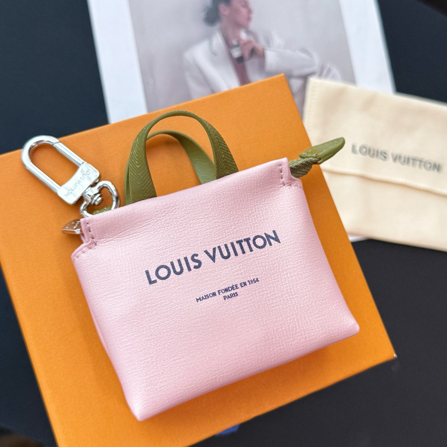 Pink small leather bag with green handle, silver zip, and Louis Vuitton logo on front.