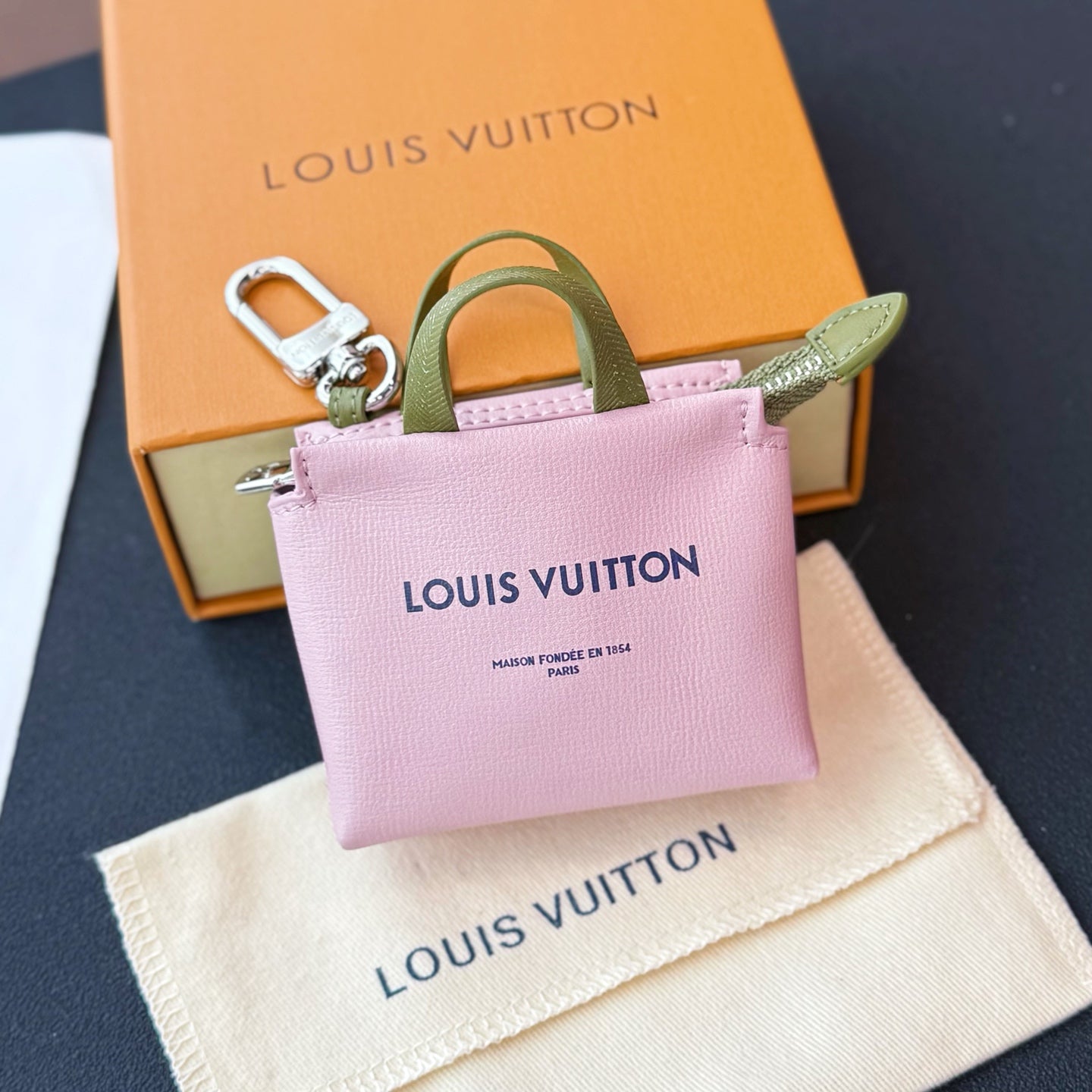 Pink small bag with green handle, silver zipper, and Louis Vuitton logo on the front.