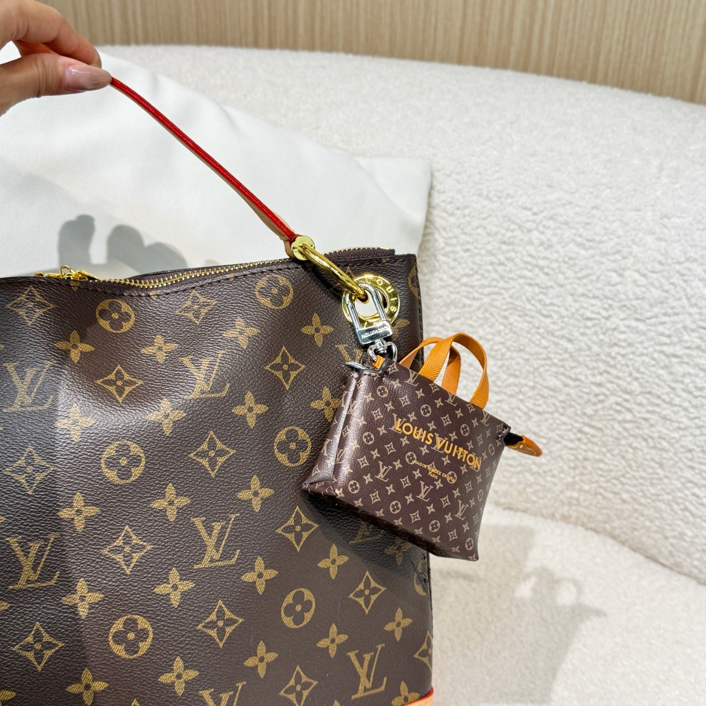 Brown monogram handbag with red zipper pull and small brown pouch charm