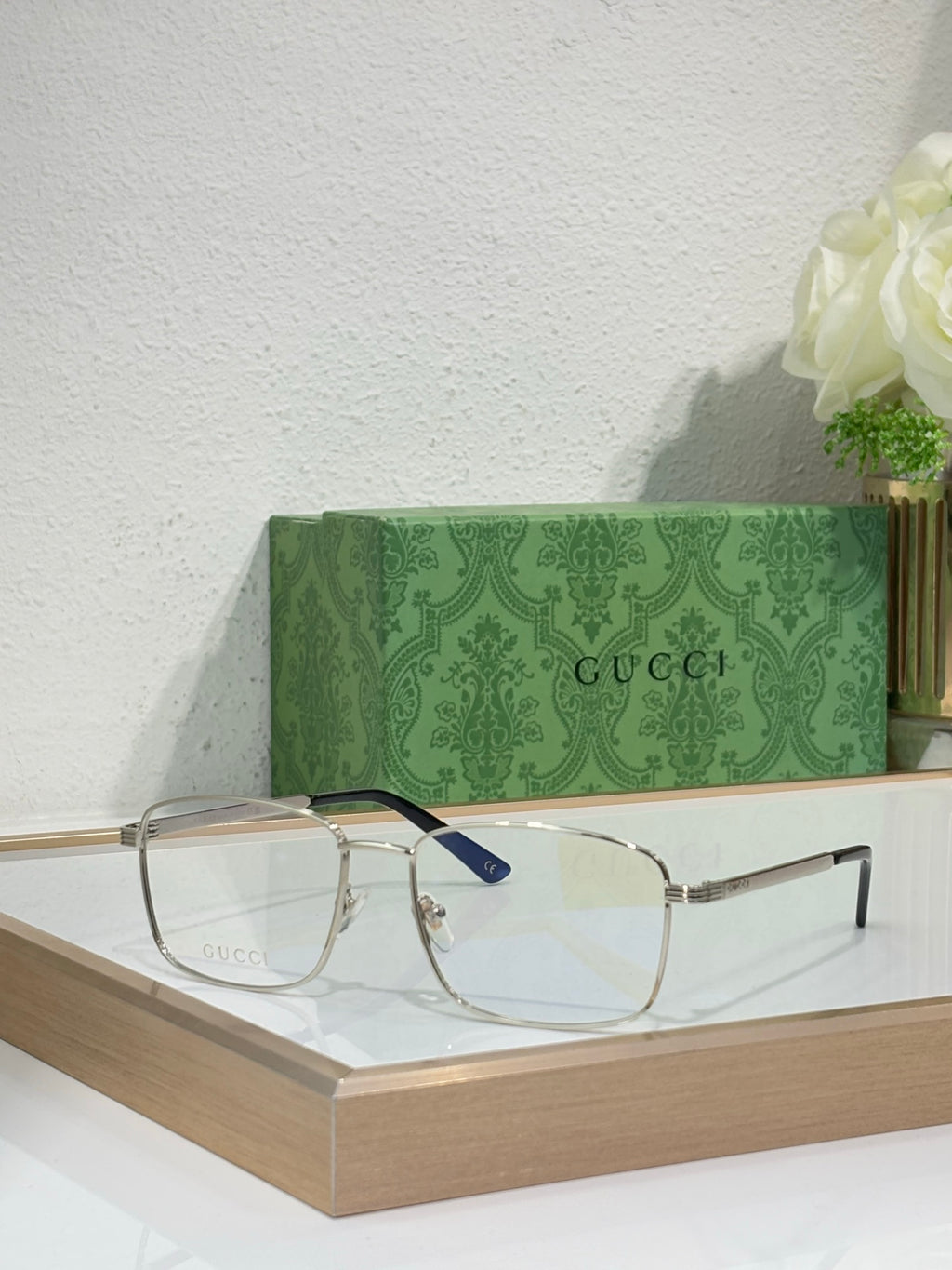Eyeglasses with gold metal rectangular frame, clear lenses, and dark blue temple detail